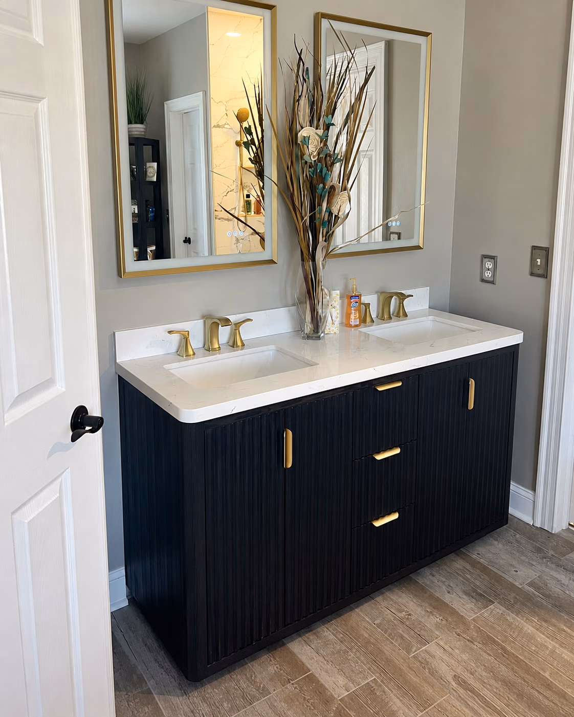Modern double bathroom vanity with black cabinet, white marble countertop, gold faucets, and two gold-framed mirrors.