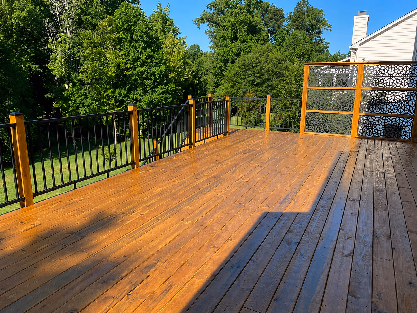 Spacious wooden deck with black metal railings and decorative privacy panels, overlooking a green yard.