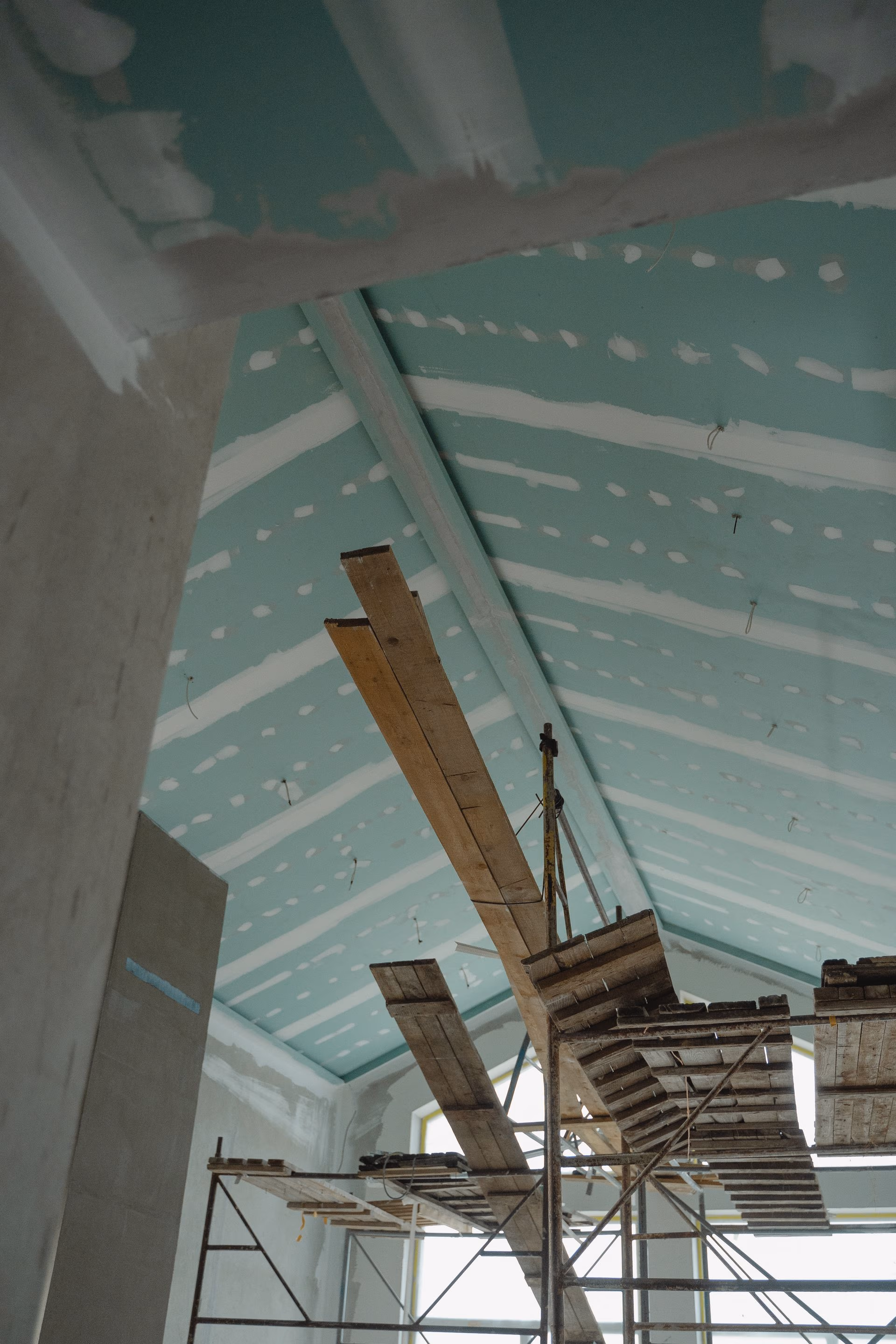 Scaffolding inside a building under construction with a ceiling partially finished with drywall panels and joint compound.