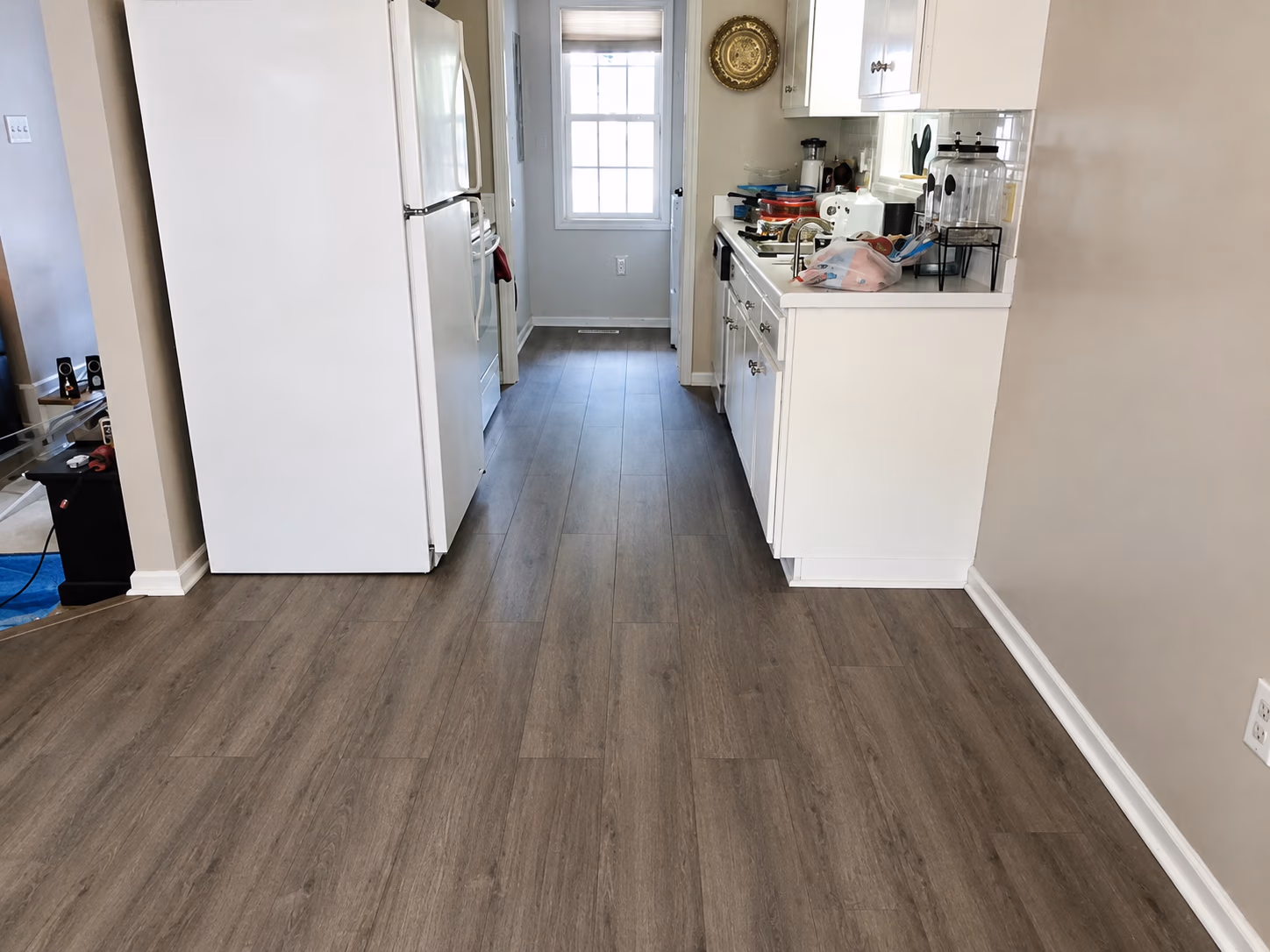 Narrow kitchen with white cabinets, white refrigerator, and wood-look flooring.
