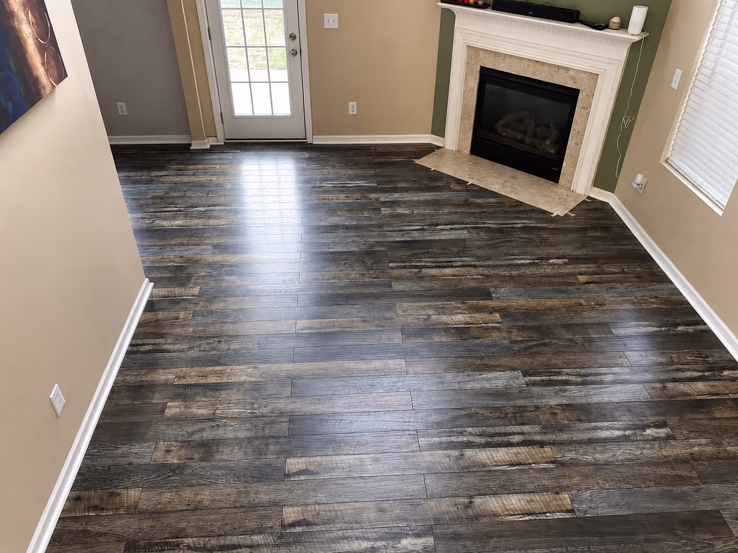 Empty room with dark wood flooring, a white-trimmed fireplace, and a glass door leading outside.