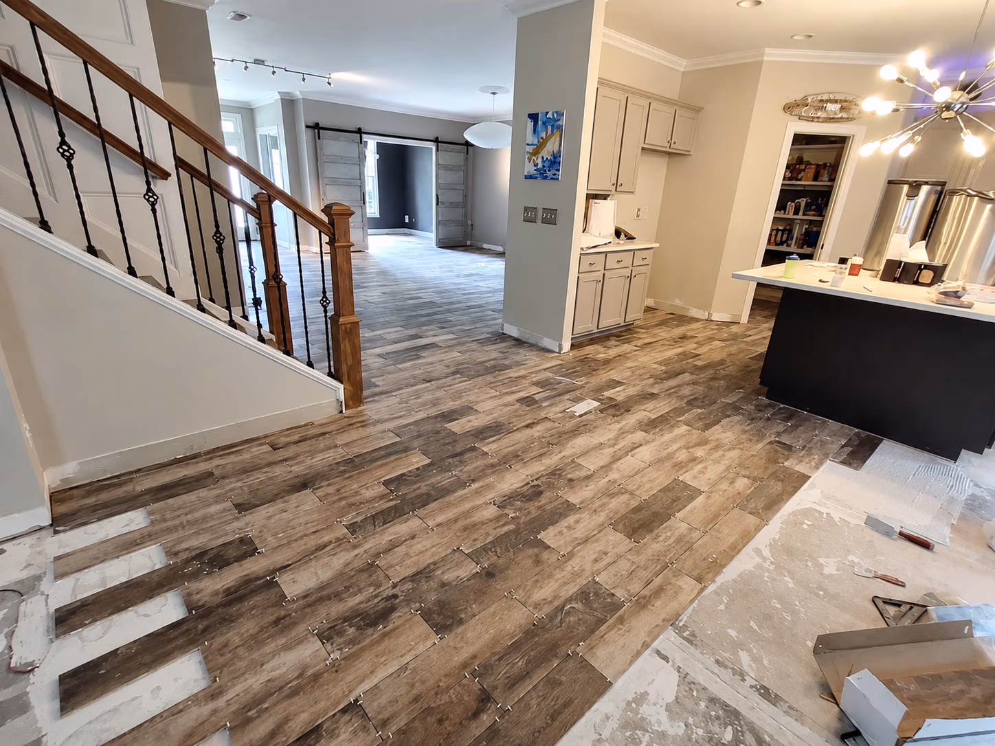 Open kitchen and living area with wood tile flooring partially installed and stair railing on left.