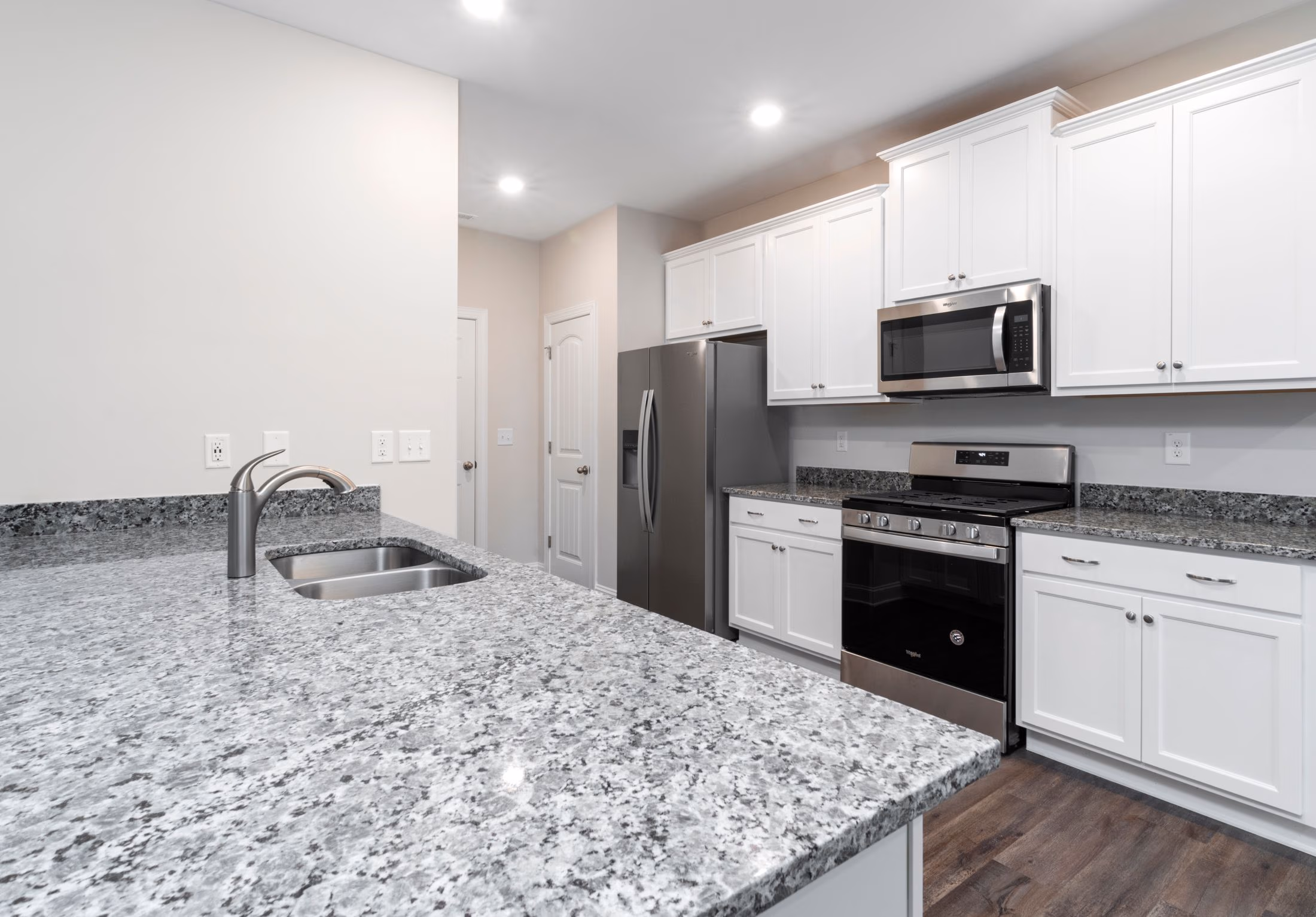 Modern kitchen with granite countertops, stainless steel appliances, white cabinets, and wooden floor.