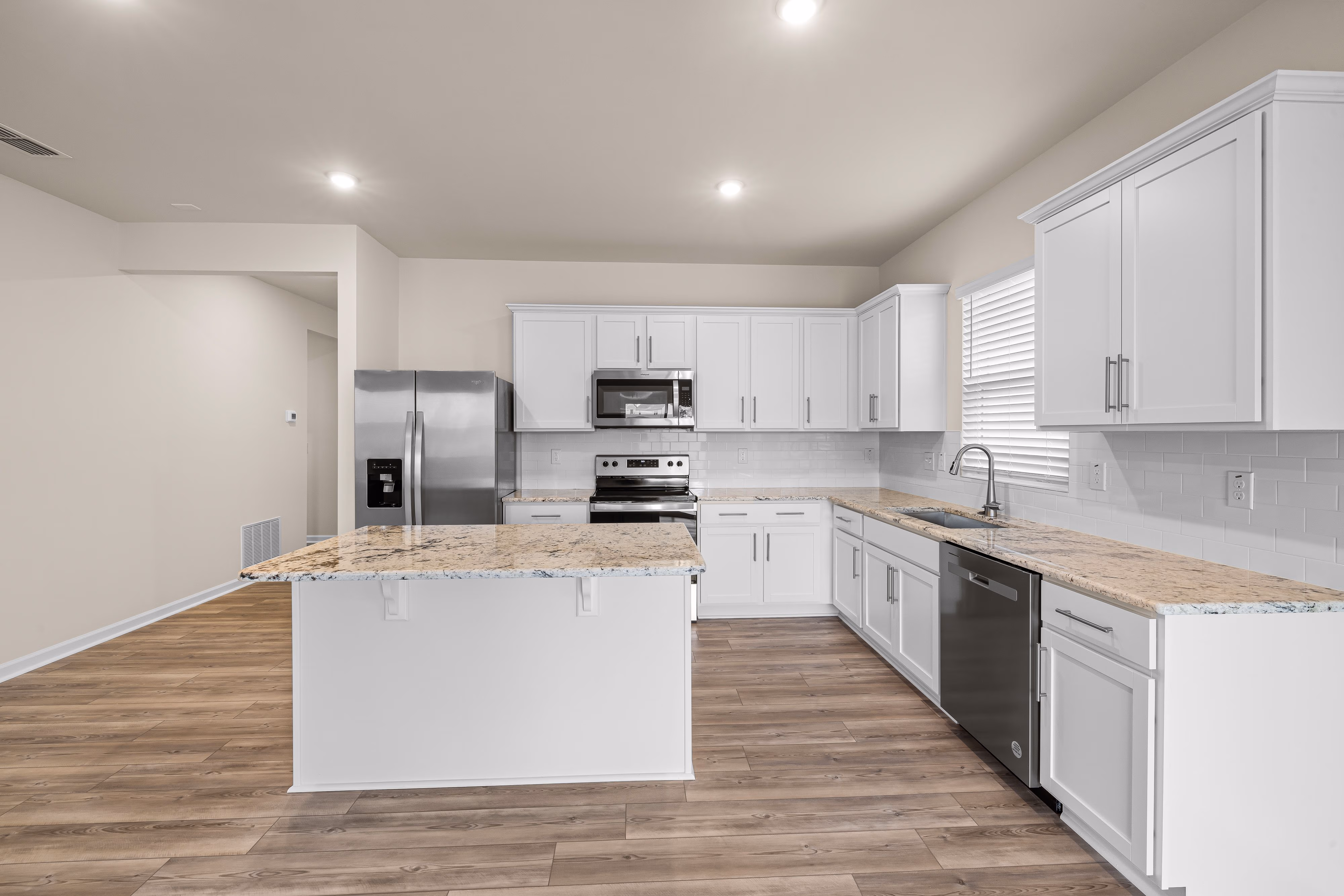 Modern kitchen with white cabinets, granite countertops, stainless steel appliances, and wood flooring.