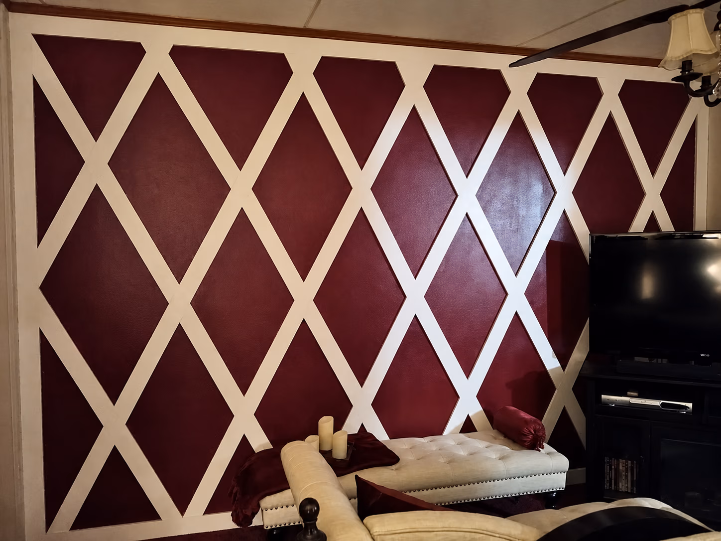 Living room wall with white crisscross pattern on burgundy, cream bench, and TV on black stand.