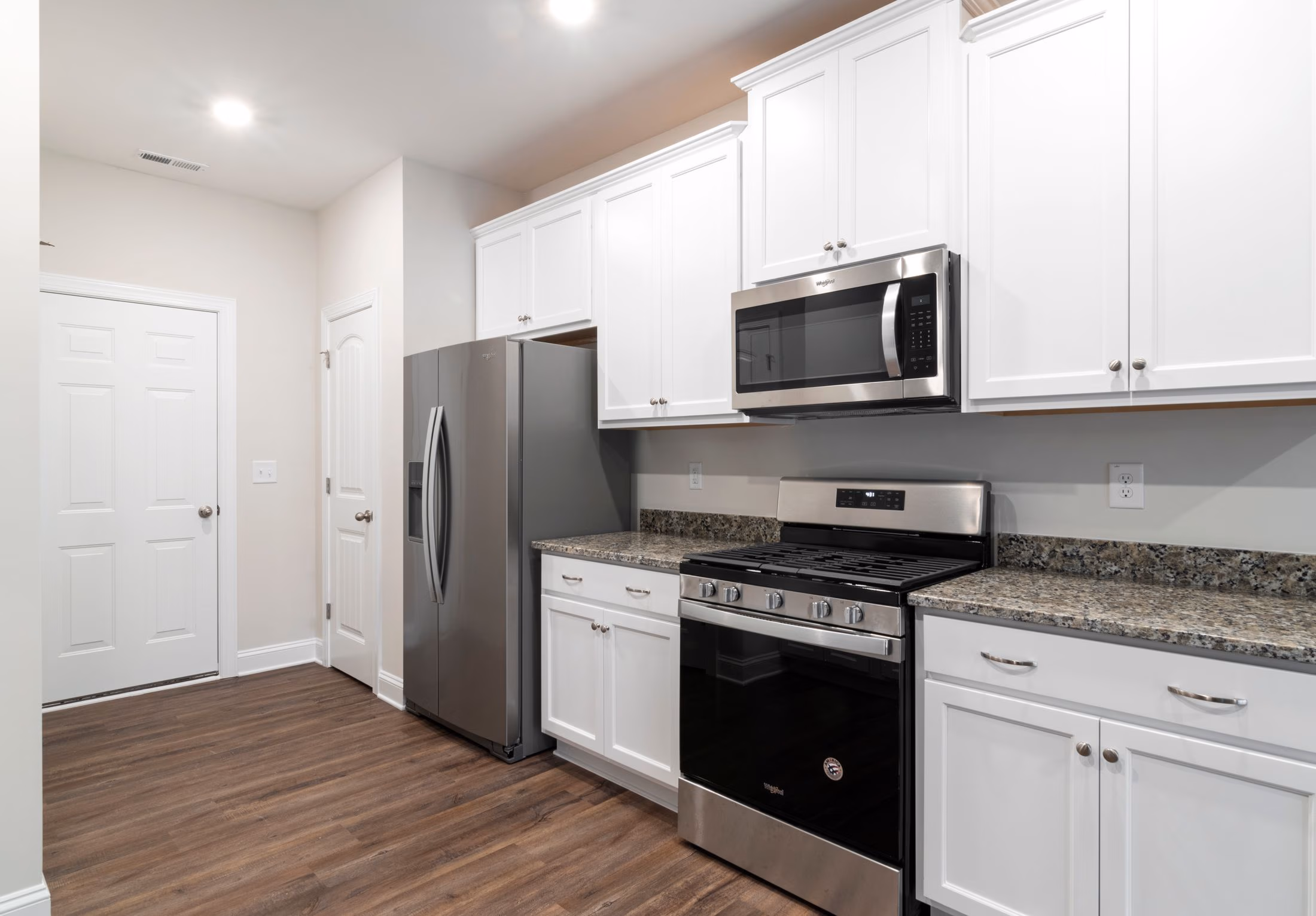 Modern kitchen with white cabinets, granite countertops, stainless steel refrigerator, stove, and microwave.