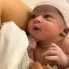 Newborn baby swaddled in a blanket, looking up while being held close.