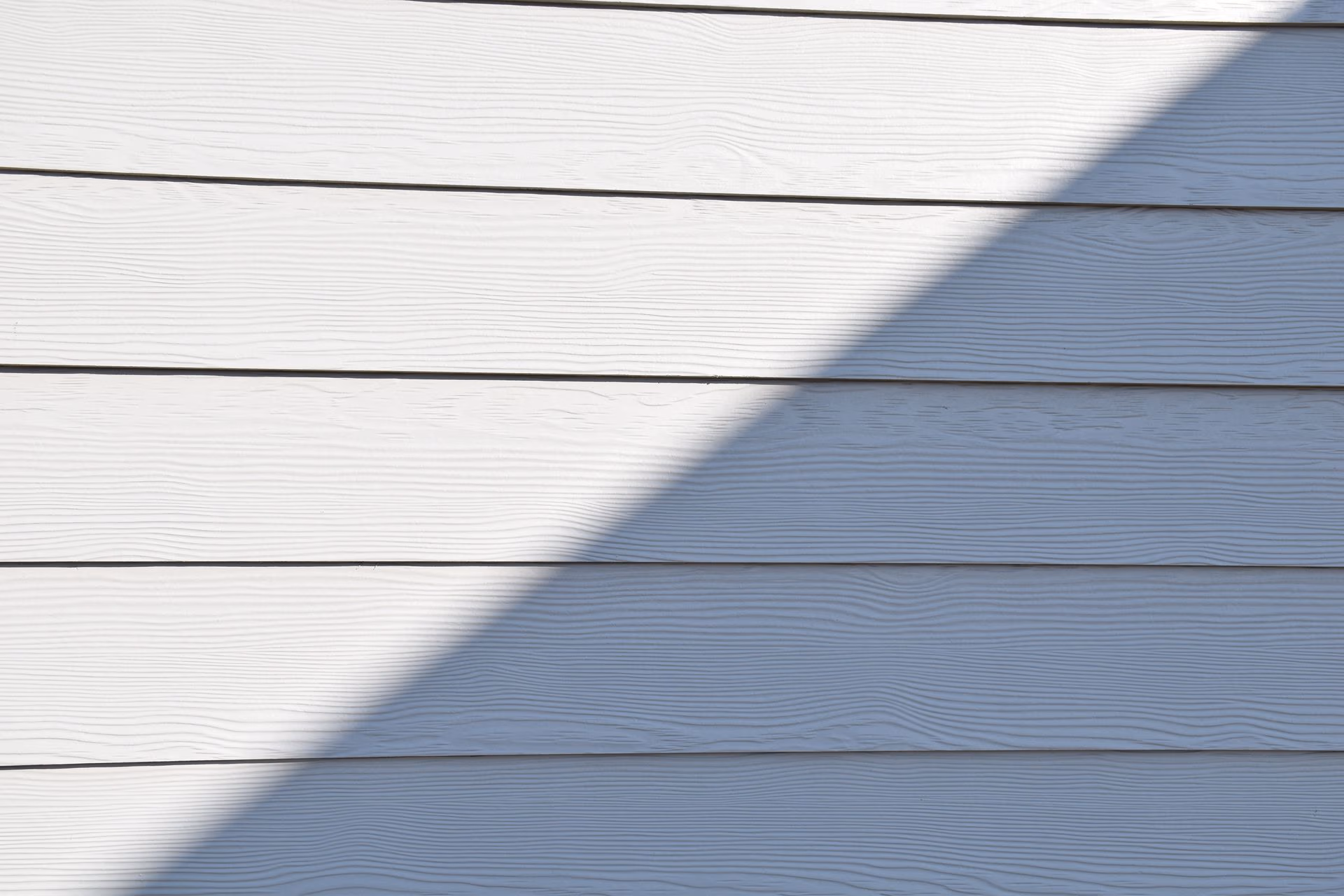 White horizontal wood siding panels with visible grain texture and a diagonal shadow across them.